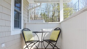 A covered patio with two metal chairs and a small table, white siding walls, and a window. - Charming Beachside Cottage: 3-Bedroom Retreat Steps from Sand, Shops & Dining! (Ogunquit)