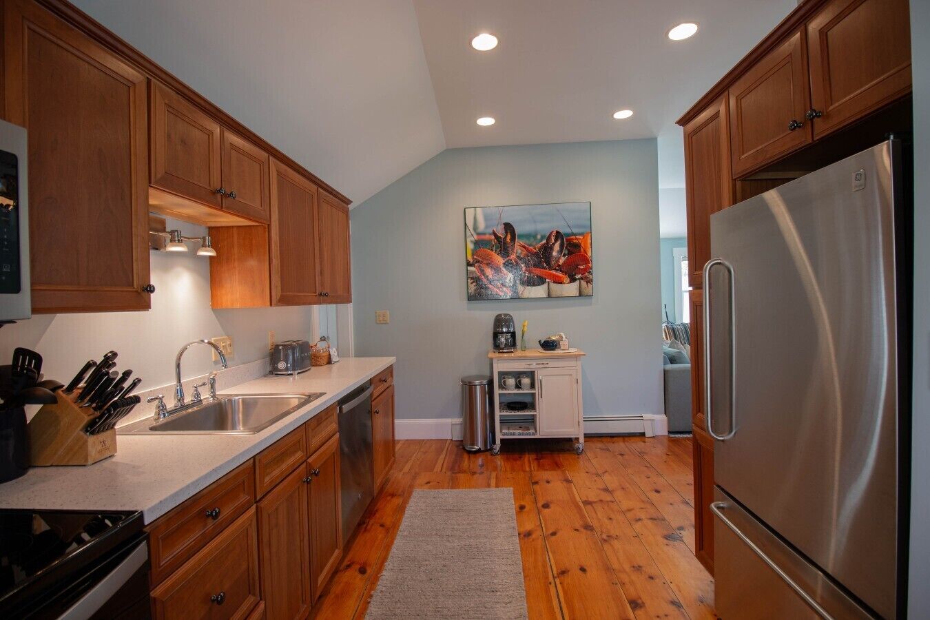 A kitchen with wooden cabinets, stainless steel appliances, a coffee maker, and a painting on the wall.
