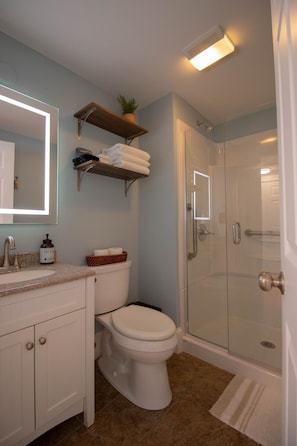 A bathroom with a toilet, sink, mirror, shower, and towel rack.