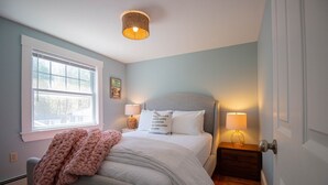 A bedroom with a bed, two bedside lamps, a window, a door, and a wall-mounted light fixture. - Charming Beachside Cottage: 3-Bedroom Retreat Steps from Sand, Shops & Dining! (Ogunquit)