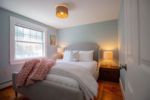 Un dormitorio con cama, dos lámparas de noche, una ventana, una puerta y una lámpara fijada a la pared.