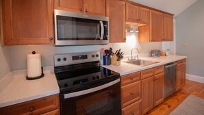 A modern kitchen with wooden cabinets, stainless steel appliances, and a white countertop. - Charming Beachside Cottage: 3-Bedroom Retreat Steps from Sand, Shops & Dining! (Ogunquit)