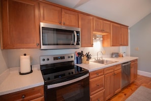 A modern kitchen with wooden cabinets, stainless steel appliances, and a countertop with a paper towel holder and knife block.