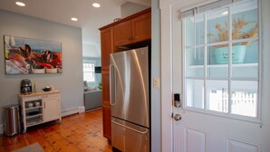 A kitchen with wooden cabinets, a stainless steel refrigerator, a coffee maker, and a painting on the wall. - Charming Beachside Cottage: 3-Bedroom Retreat Steps from Sand, Shops & Dining! (Ogunquit)