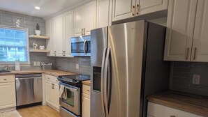 Una cocina moderna con electrodomésticos de acero inoxidable, armarios blancos y encimera de madera.
