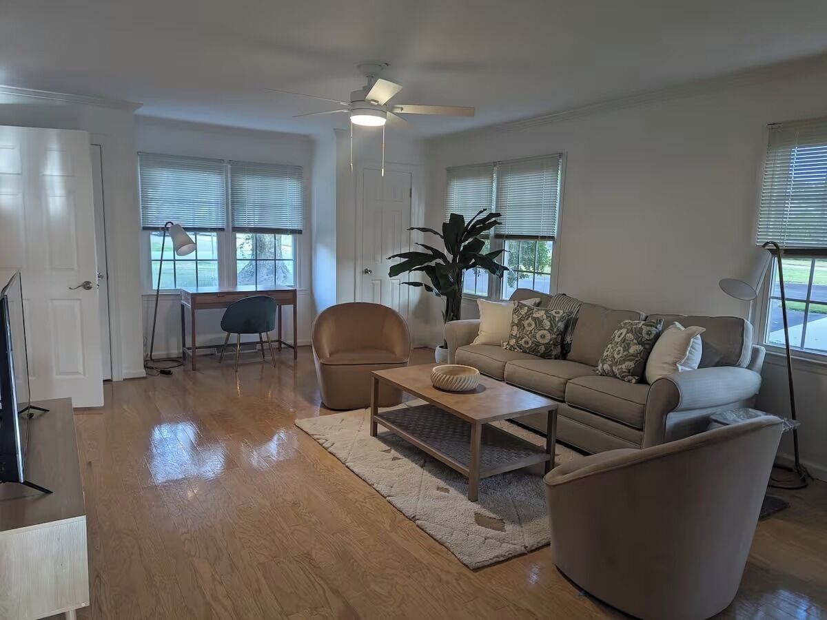 A spacious living room with a sofa, armchairs, a coffee table, and a ceiling fan.