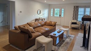 Una sala de estar moderna con un sofá de cuero marrón, un sillón blanco y una mesa de centro de madera.