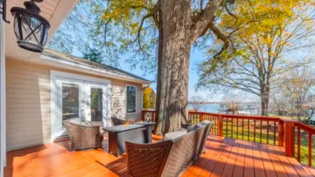 Una terraza de madera con mobiliario exterior, un árbol grande y vista al océano.