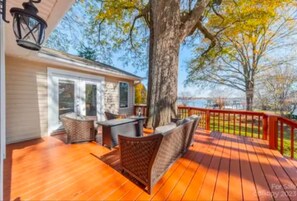 Eine Holzterrasse mit Gartenmöbeln, ein großer Baum und Blick auf den Ozean.