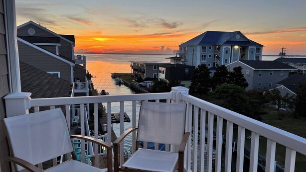 A balcony with two chairs overlooking a waterfront with buildings and a sunset. - Luxury Waterfront Oasis with Pool & Beach Access (Ocean City)