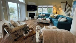 A spacious living room with a large TV, a fireplace, a blue sofa, and a balcony with a view. - Luxury Waterfront Oasis with Pool & Beach Access (Ocean City)