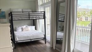 A bedroom with a bunk bed, a bedside table, a dresser, and a view of the outside. - Luxury Waterfront Oasis with Pool & Beach Access (Ocean City)