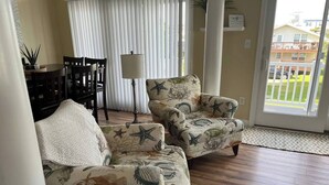 A living room with two armchairs featuring a sea-themed pattern, a dining table with chairs, a lamp, and a view of the outside through large windows. - Luxury Waterfront Oasis with Pool & Beach Access (Ocean City)