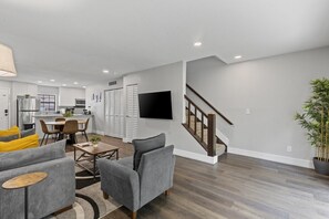 A modern living room with a grey sofa, a coffee table, and a dining area with chairs and a table.