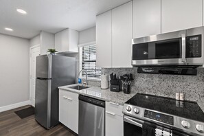 A modern kitchen with stainless steel appliances, a granite countertop, and white cabinetry.