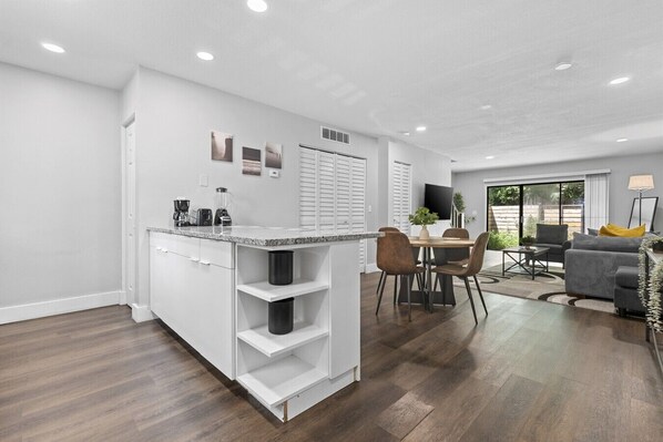 A modern kitchen with a dining area, a TV, and a sofa in a bright living space.