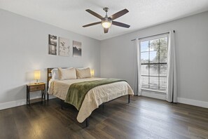 Un dormitorio con cama, lámparas de noche, ventilador de techo y ventana con persianas.