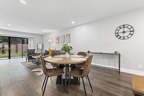 A modern dining area with a round table, chairs, and a wall-mounted clock.