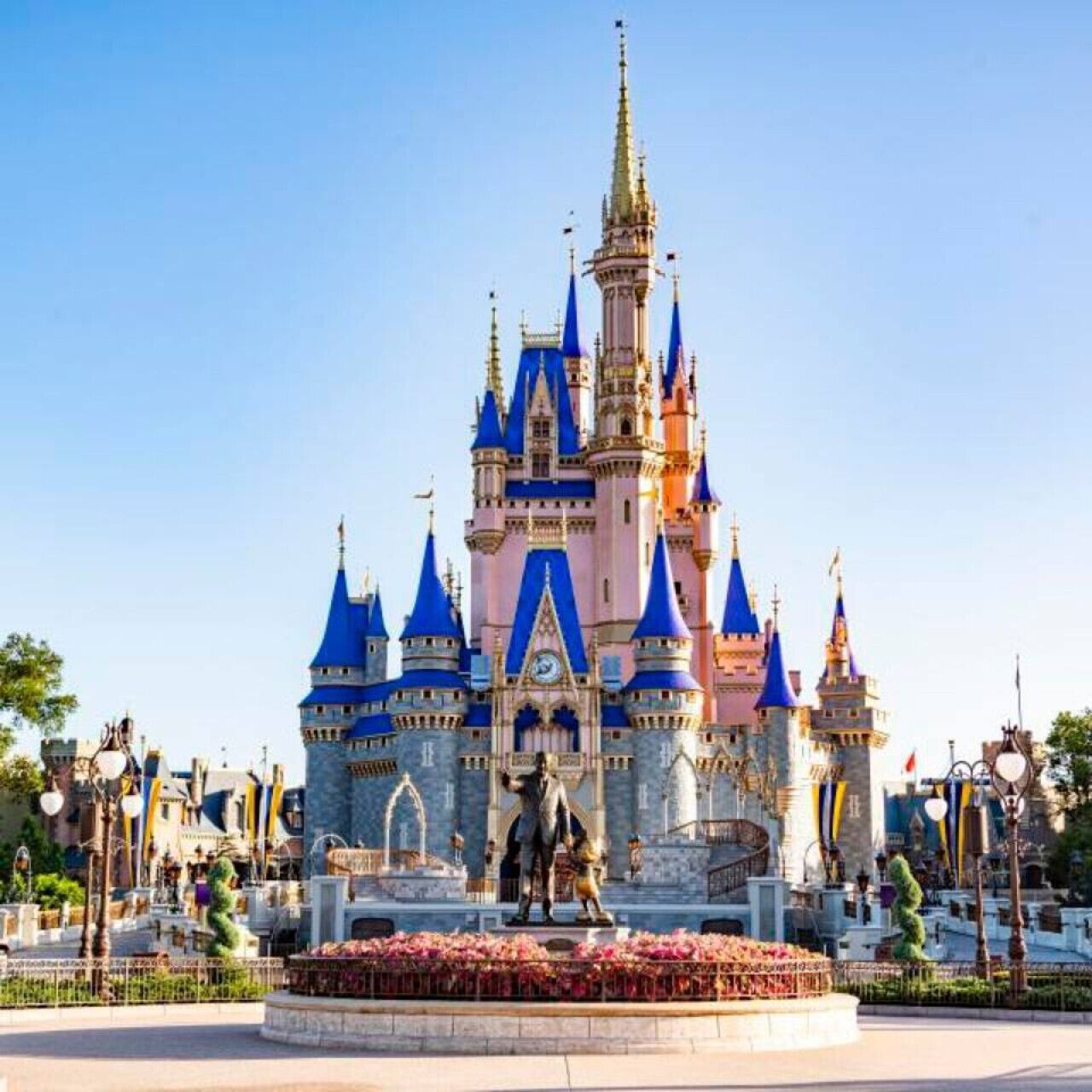 A castle with multiple spires and a central tower, surrounded by a circular flower bed and a statue.