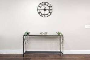 A minimalist console table with a "HOME" sign, a wall-mounted clock, and decorative plants.