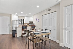 A modern kitchen with white cabinets, stainless steel appliances, and a dining area with a wooden table and metal chairs.