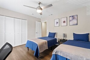 A room with two beds, a ceiling fan, and a door.
