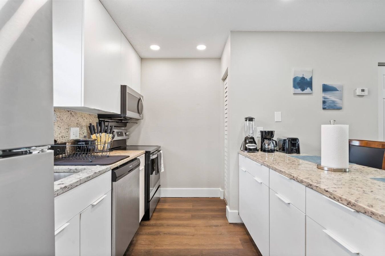A modern kitchen with white cabinets, a granite countertop, and a wooden floor.