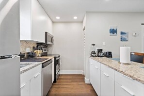 A modern kitchen with white cabinets, a granite countertop, and a wooden floor.