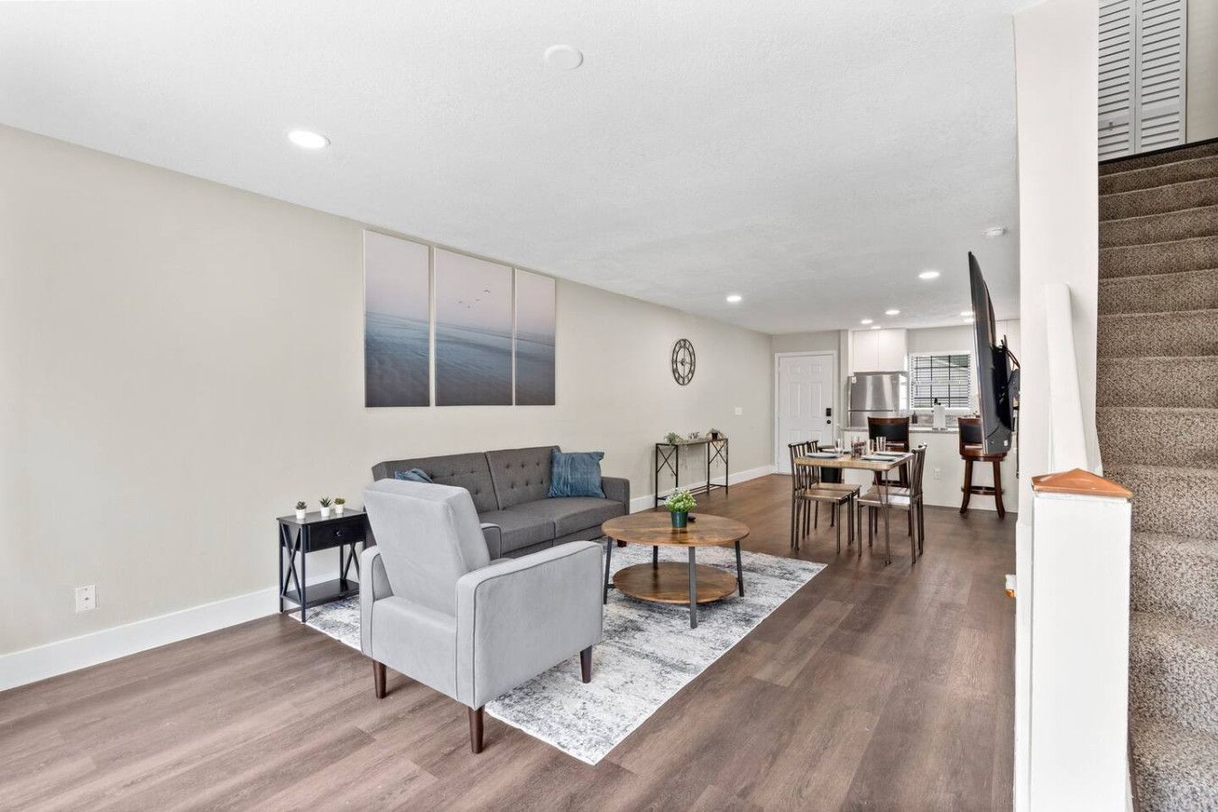 A modern living room with a grey sofa, a coffee table, and a dining area with a kitchen in the background.