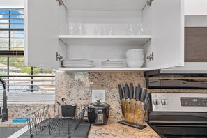 A kitchen with white cabinets, a granite countertop, a coffee maker, a rice cooker, and a knife block.