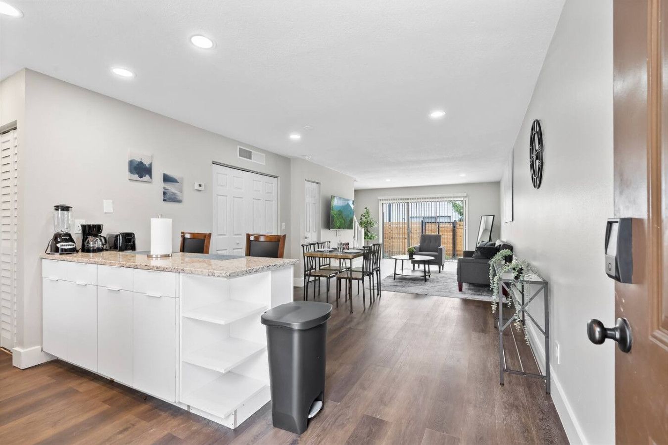 A modern kitchen with white cabinets, a granite countertop, and a dining area with a table and chairs.