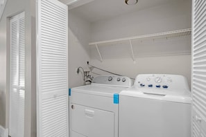 Ein Waschraum mit einer Frontlader-Waschmaschine und -trockner, einem Metallregal und einer Tür mit abgefasten Glasscheiben.