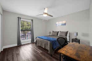 A bedroom with a bed, a desk, a chair, a ceiling fan, a window with blinds, and a painting on the wall. - Tampa's Peaceful Retreat (Tampa)