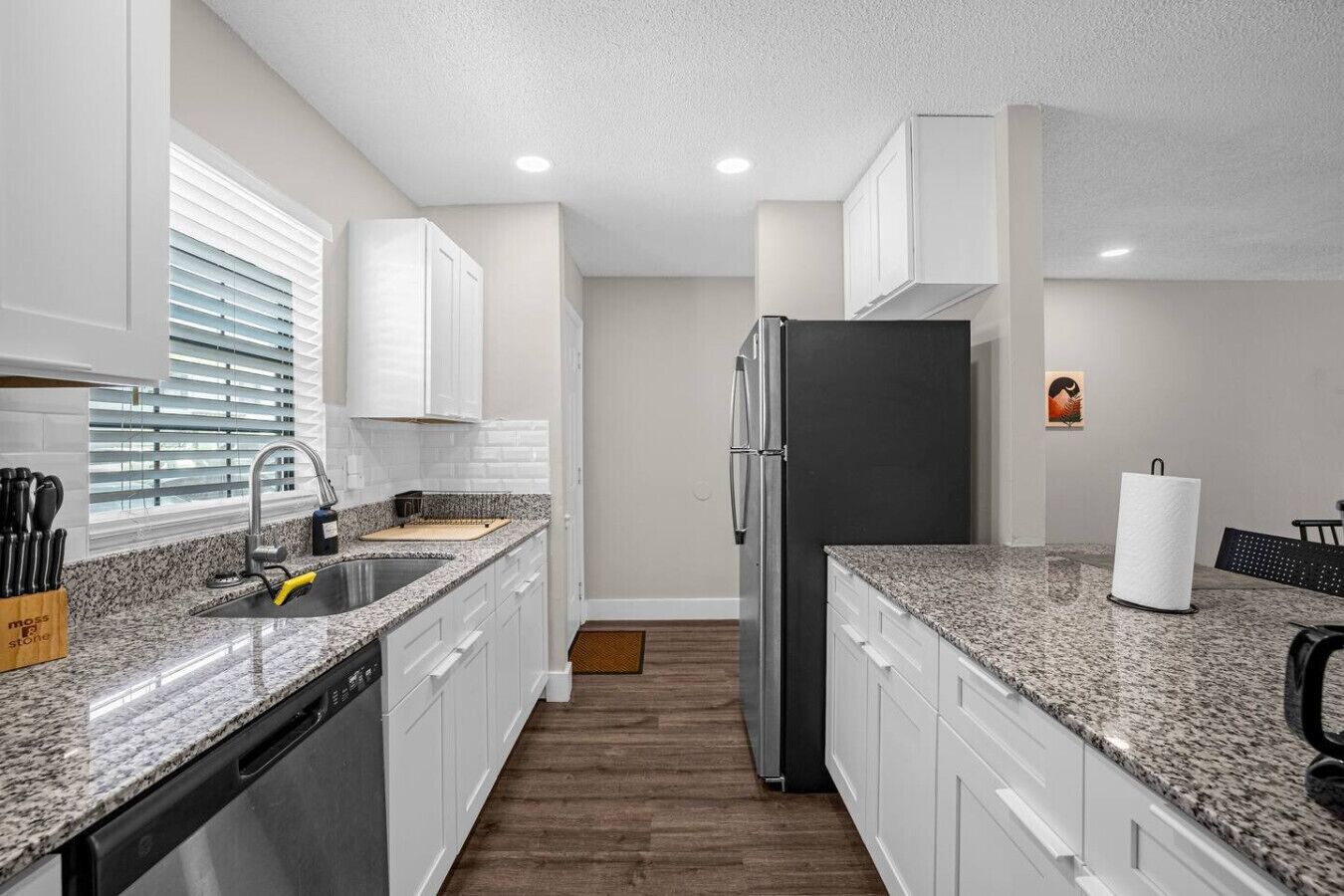 Eine moderne Küche mit weißen Schränken, Granit Arbeitsplatten, einem Edelstahlkühlschrank und einem Geschirrspüler.
