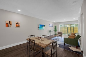 Ein modernes Wohnzimmer mit Essbereich, mit einem Holztisch und Stühlen, einem grünen Sofa und Kunstwerken an den Wänden.
