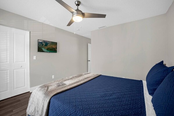 A bedroom with a bed, a ceiling fan, a painting on the wall, and a door.