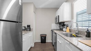 A modern kitchen with stainless steel appliances, white cabinets, granite countertops, and a black trash bin.