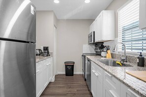 A modern kitchen with stainless steel appliances, white cabinets, granite countertops, and a black trash bin. - Tampa's Peaceful Retreat (Tampa)