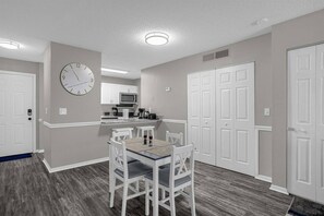 A compact kitchen with white cabinets, a microwave, and a clock on the wall.