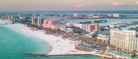 A coastal cityscape with a beachfront hotel, a sandy beach, and a marina.