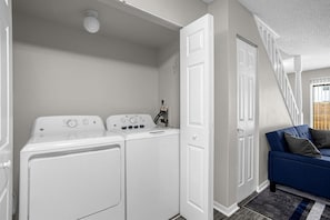 A laundry room with two white washing machines, a door, and a blue sofa with a striped rug.