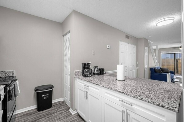 A kitchen with white cabinets, a granite countertop, a coffee maker, and a trash can.