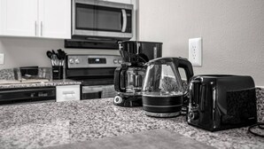 Et køkken med mikroovn, kaffemaskine, elkedel og brødrister på en granitbordplade.