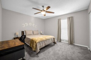 A bedroom with a bed, a desk, a chair, a ceiling fan, and a window with curtains.