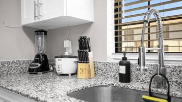 Una cocina con encimera de granito, batidora, olla de cocción lenta, bloque de cuchillos, botella de detergente y pileta de acero inoxidable con grifo.
