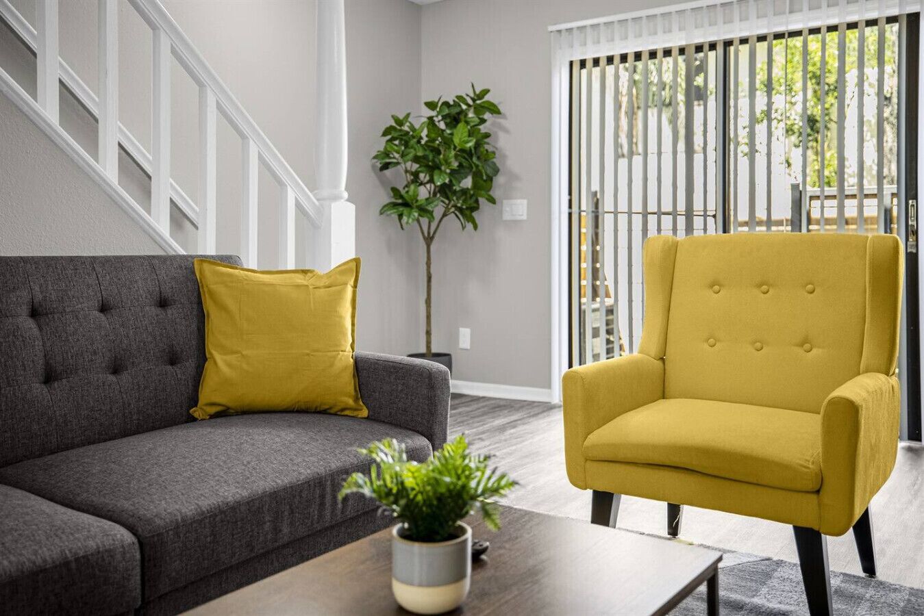 A living room with a grey sofa, a yellow armchair, and a potted plant on a wooden coffee table.