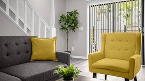 A living room with a grey sofa, a yellow armchair, and a potted plant on a wooden coffee table. - Sunshine Retreat Minutes from Moffit, USF, and Busch Gardens (Tampa)