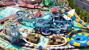 Un parc aquatique doté de nombreux toboggans et de plusieurs piscines, entouré d’immeubles et bordé par une route.