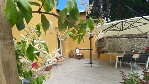 An outdoor patio area with a stone floor, a dining table with chairs, and potted plants with white flowers.