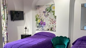 A bedroom with two beds, a green chair, a TV, and a floral wall art piece.